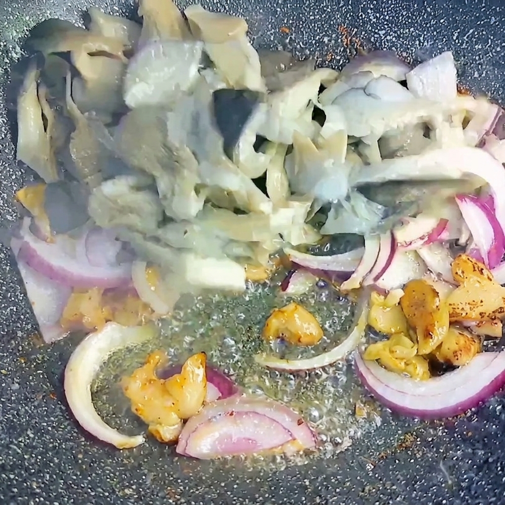 Blanchierte Austernpilze und in Scheiben geschnittene rote Zwiebeln werden zusammen mit den knusprigen Schweinebauchstücken im Wok geschwenkt.