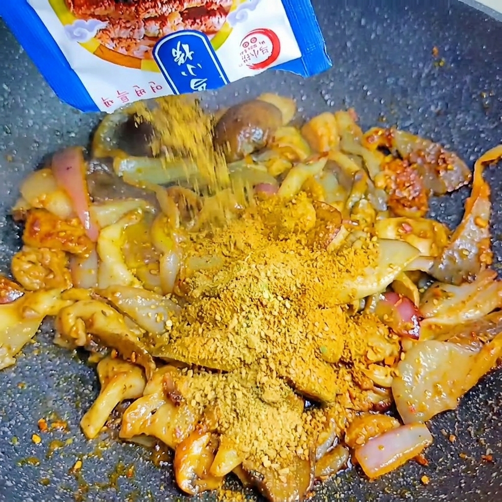 Aus einer blauen Packung wird koreanisches BBQ-Gewürzpulver über die Pilze und Zwiebeln im heißen Wok gestreut.