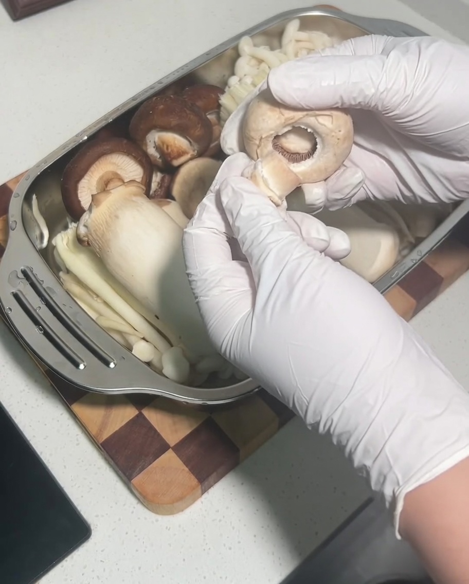 Eine Hand entfernt den Stiel von einem rohen Shiitake-Pilzkopf.
