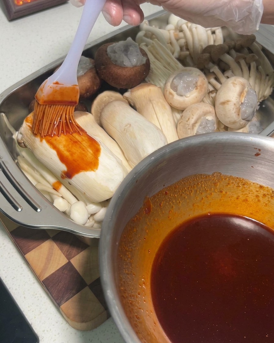 Sauce wird mit einem Pinsel auf rohe Kräuterseitlinge in einer Metallschale aufgetragen.