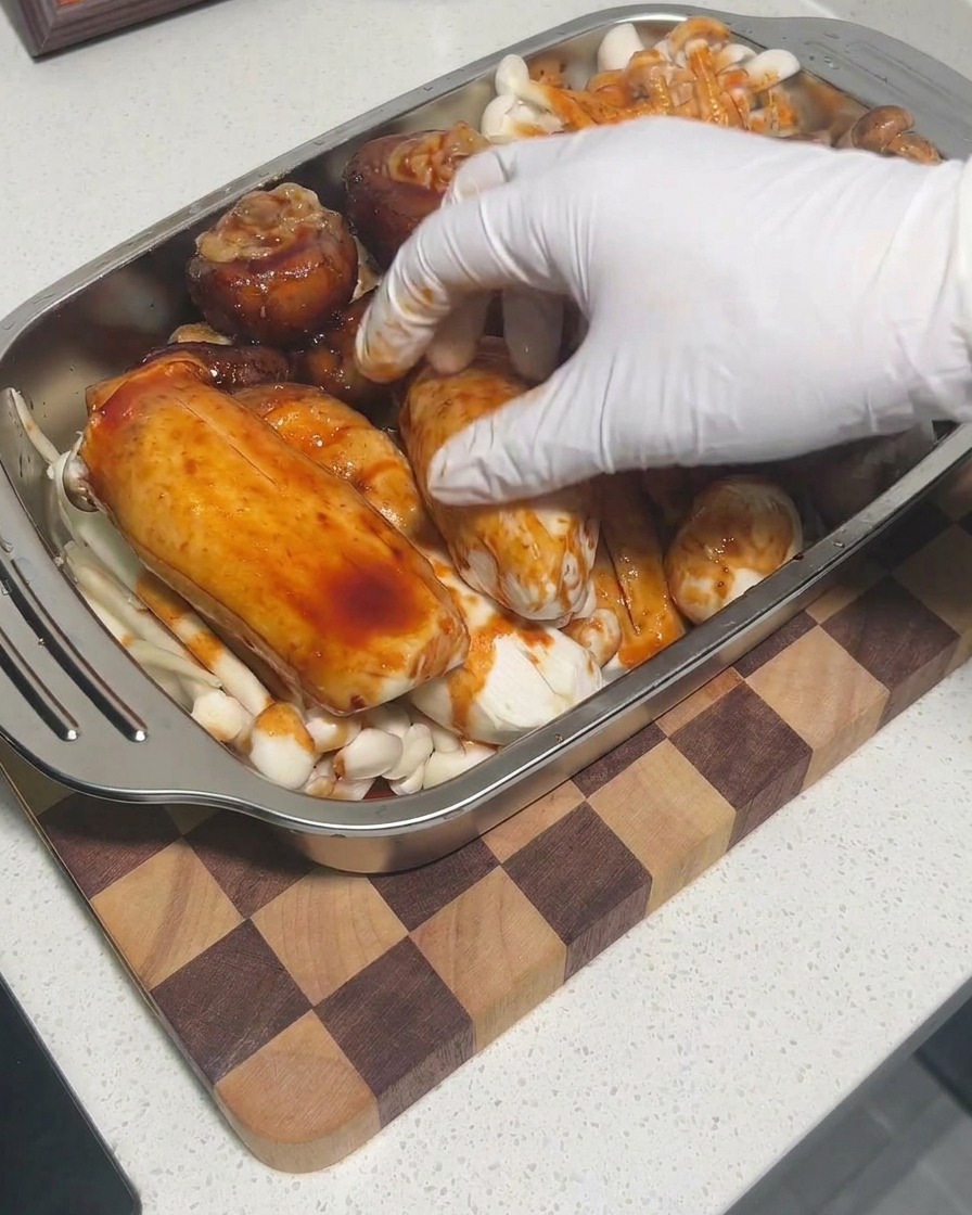 Behandschuhte Hände massieren Sauce in die Pilze in einer Schale ein.