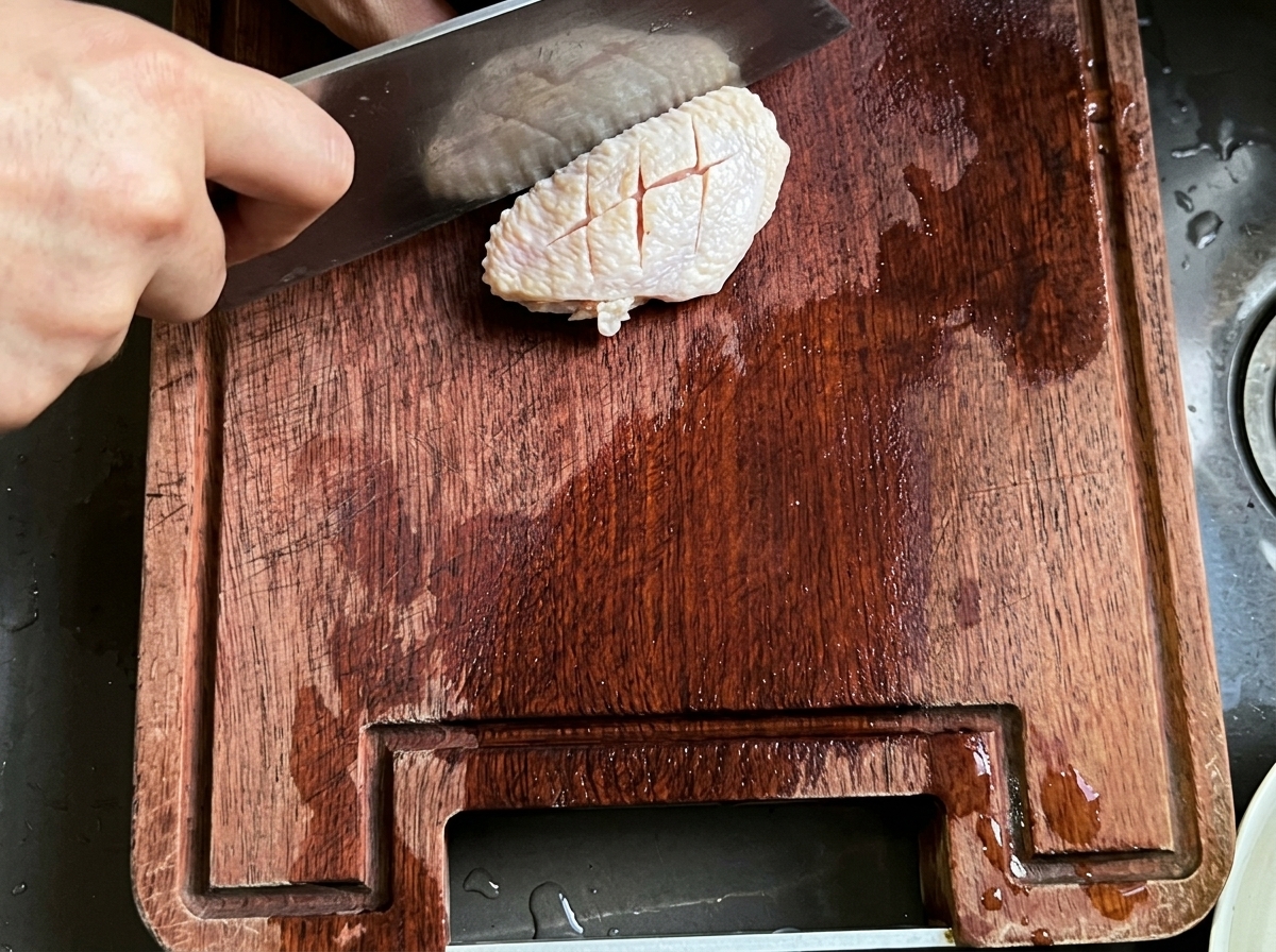 Ein roher Hähnchenflügel wird mit einem Fleischbeil auf einem Holzschneidebrett eingeritzt.