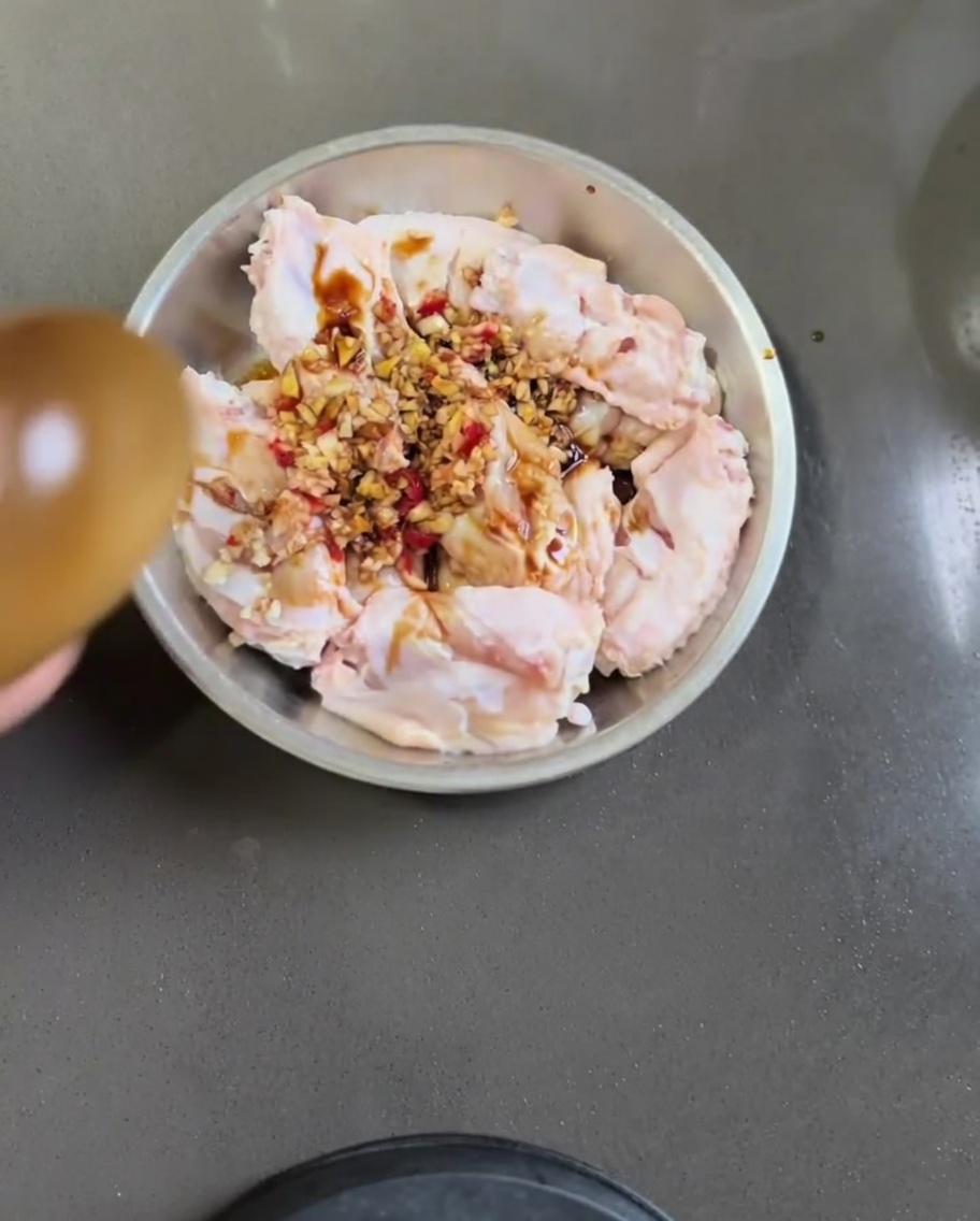 Rohe Hähnchenflügel in einer Metallschüssel, vermischt mit Knoblauch, Chili, Sojasauce und Sesamöl.