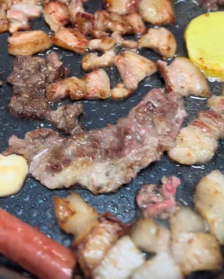 Schweinebauch, Champignonköpfe und Kartoffelscheiben brutzeln auf einem Elektrogrill mit schöner goldbrauner Kruste.