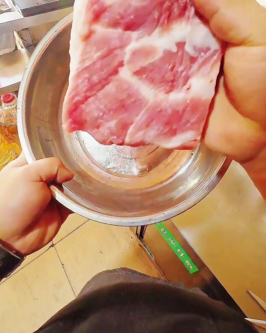 Ein scharfes Messer schneidet einen frischen, rohen Schweinebauch auf einem Holzschneidebrett.