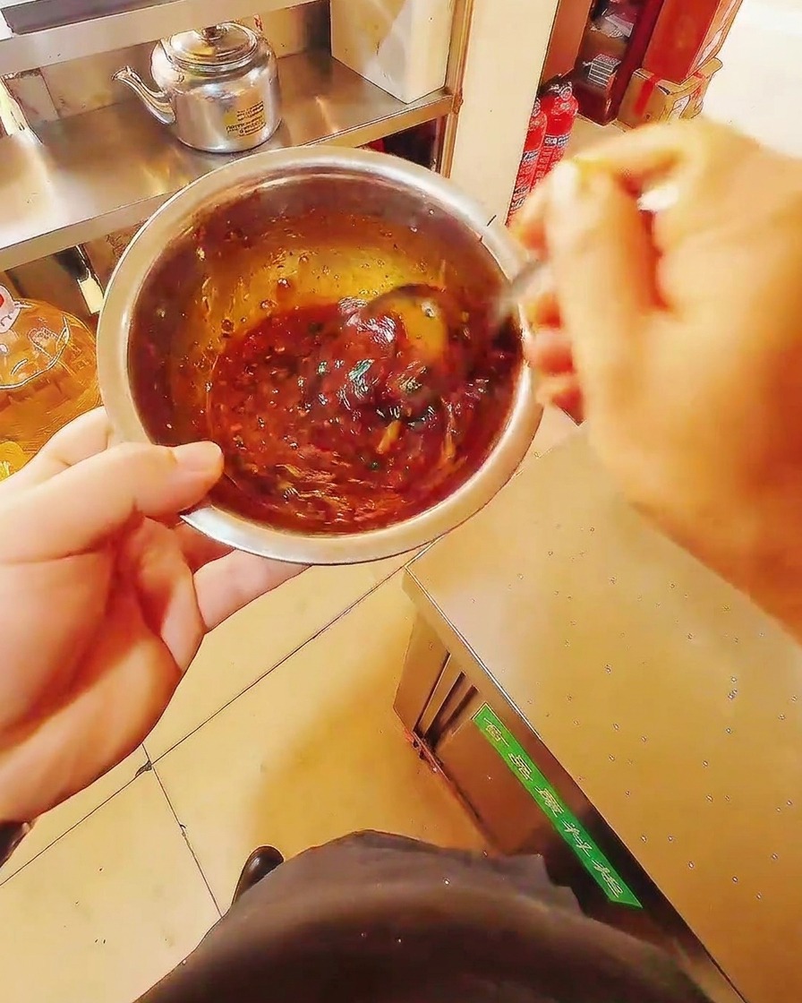 Nahaufnahme einer Edelstahlschüssel mit einer reichhaltigen, dunkelroten Marinade, die mit einem Metalllöffel verrührt wird.