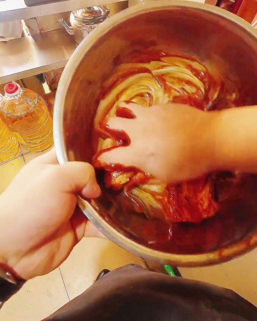 Rohe Schweinebauchstreifen werden in einer großen Schüssel mit einer dicken, glänzenden roten Marinade von Hand vermengt.