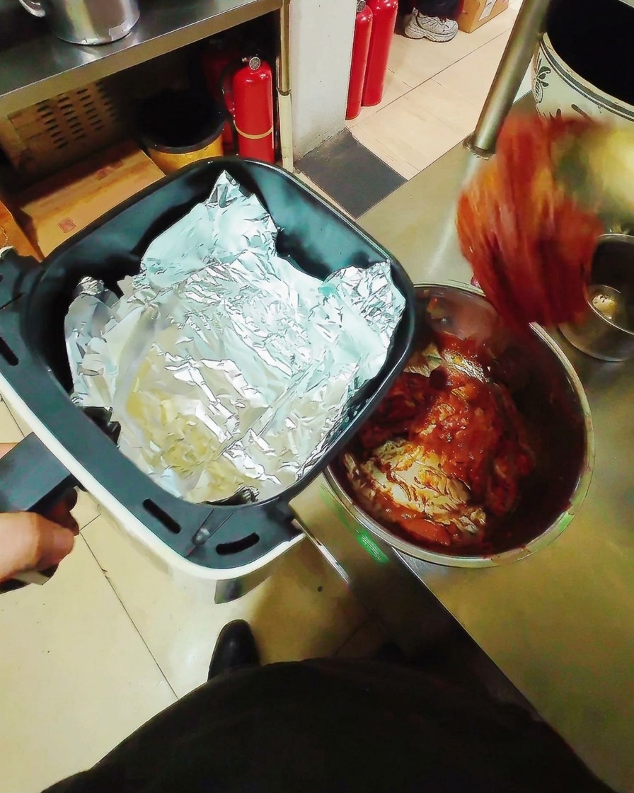 Marinierte Schweinebauchstreifen liegen flach auf Alufolie in einem Heißluftfritteusen-Korb, bereit zum Garen.