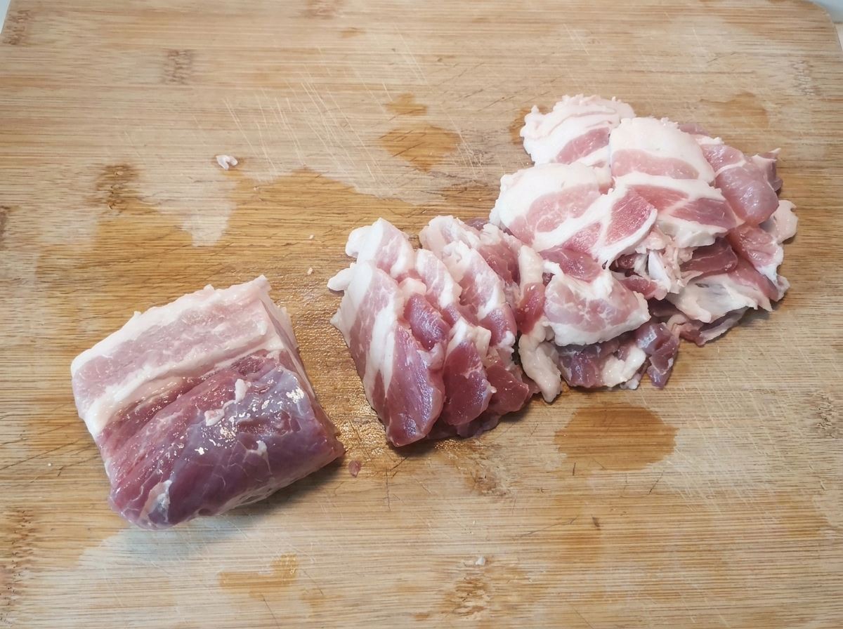 Dünne, rohe Schweinebauchscheiben, die nach dem Schneiden ordentlich auf einem Holzschneidebrett angeordnet sind.