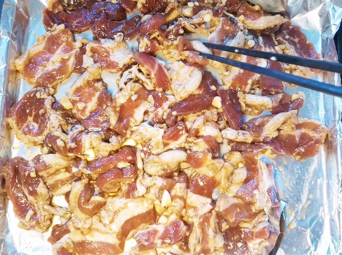 Marinierte Schweinebauchscheiben, die in einer einzigen Schicht auf einem mit Folie ausgelegten Backblech liegen.