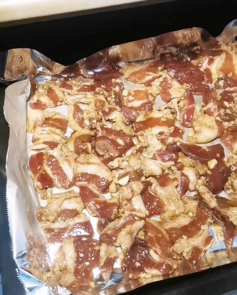 Ein Backblech mit gewürzten Schweinebauchscheiben wird in einen heißen Ofen geschoben.