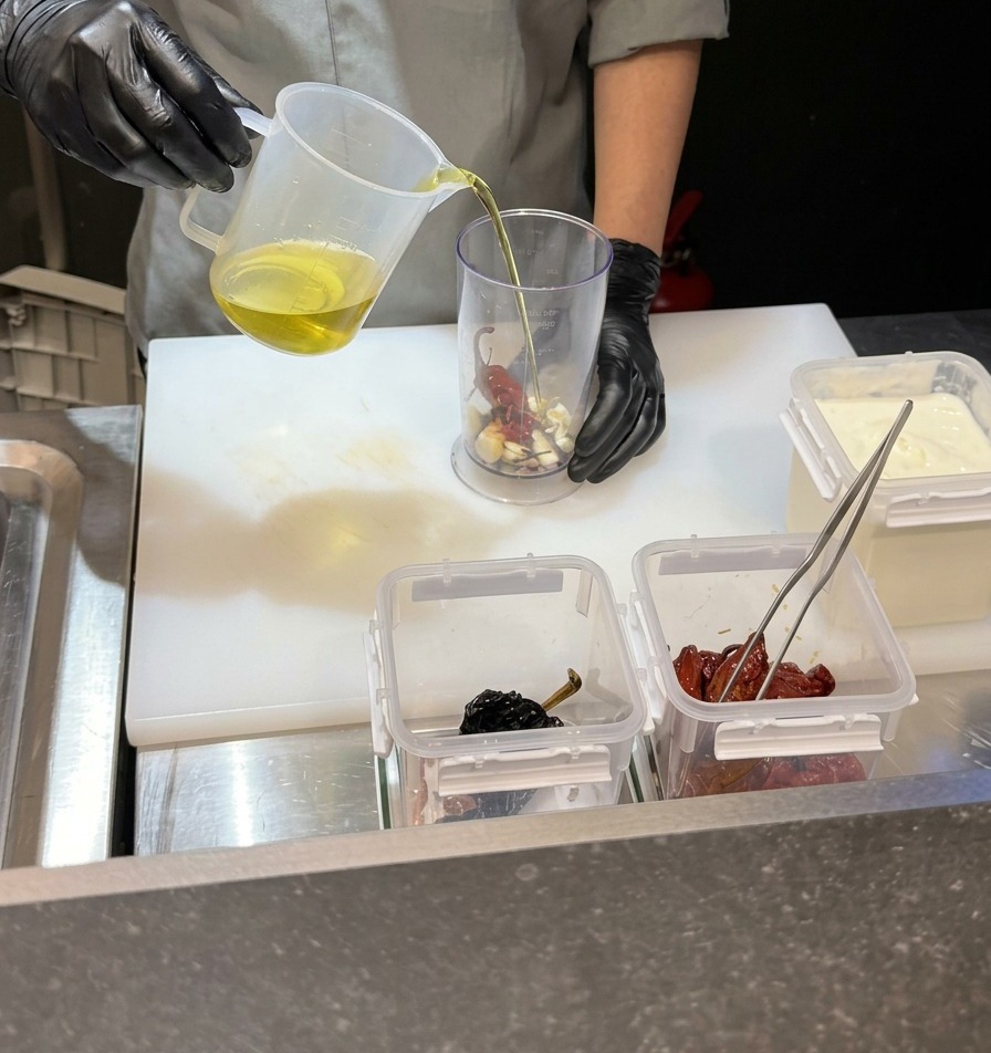 Der Koch gießt eine klare Flüssigkeit in einen hohen Mixbecher mit Knoblauch und Chilis.