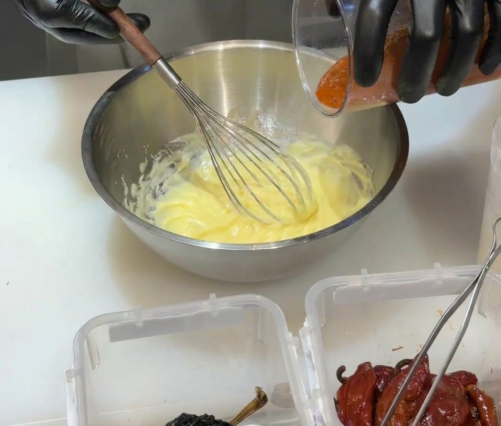 Rotes Chili-Püree wird in eine gelbe Mayonnaise-Basis in einer Metallschüssel gegossen.