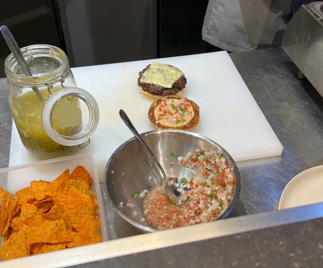 Rinderhackfleisch-Bällchen werden auf einer heißen Grillplatte mit einer Metallpresse flach gedrückt.