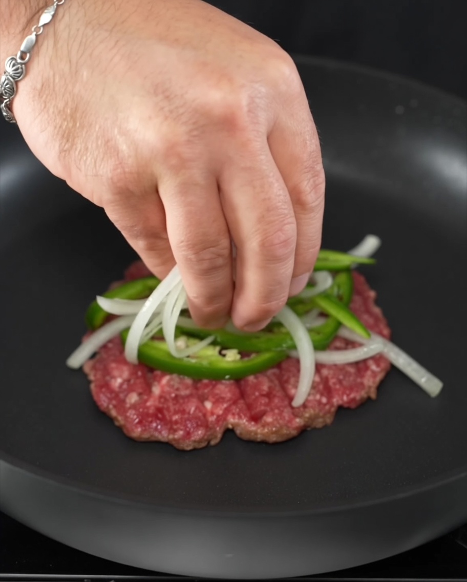Frische Jalapeño-Ringe und Zwiebelscheiben auf einem brutzelnden Rindfleisch-Patty.