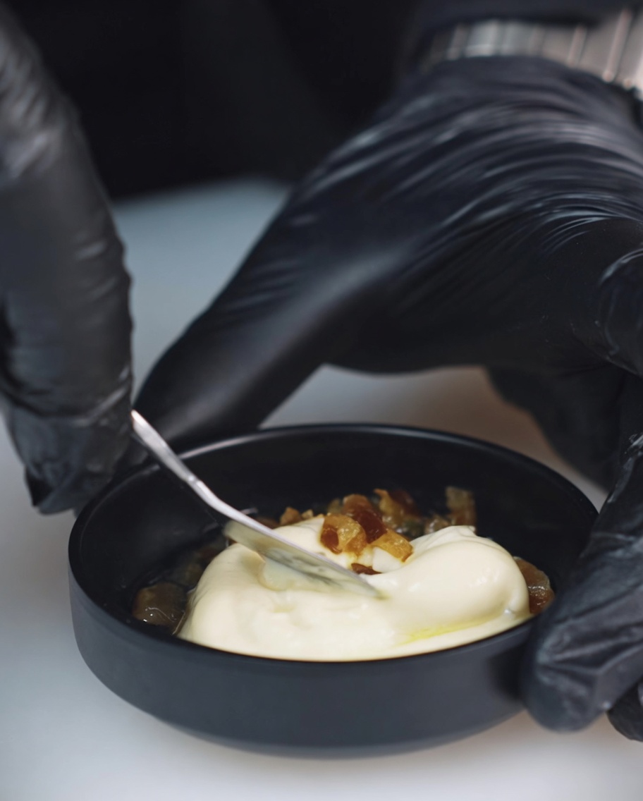 Nahaufnahme einer kleinen Schüssel, in der Mayonnaise, gehackte mexikanische Chilis und Gurkenwasser mit einem Löffel vermischt werden.