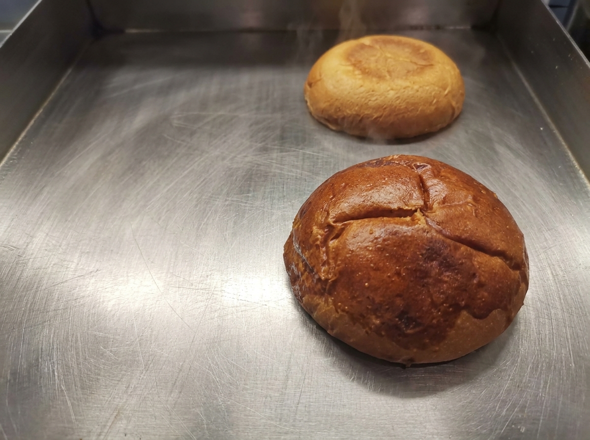 Goldbraun getoastete Burgerbrötchen-Hälften auf einer sauberen Grillplatte.