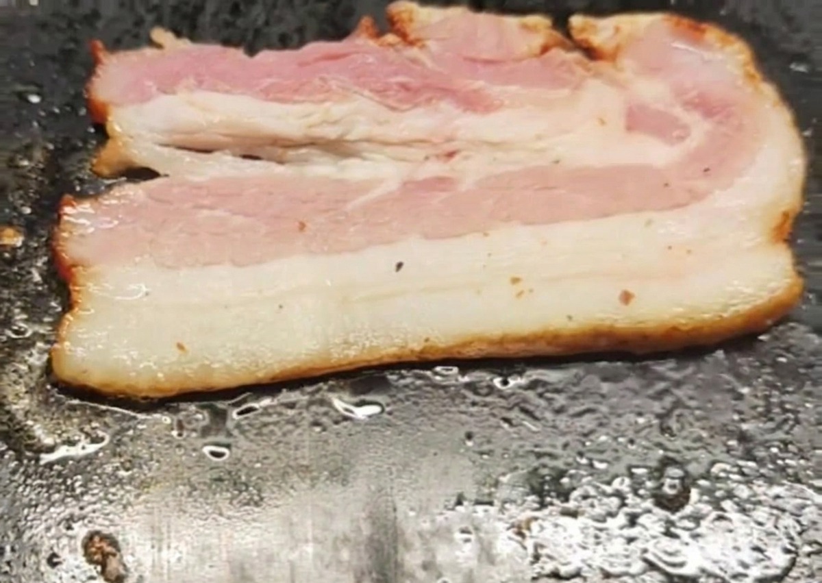 Ein einzelner Speckstreifen, der auf einer heißen, flachen Grillplatte brutzelt.