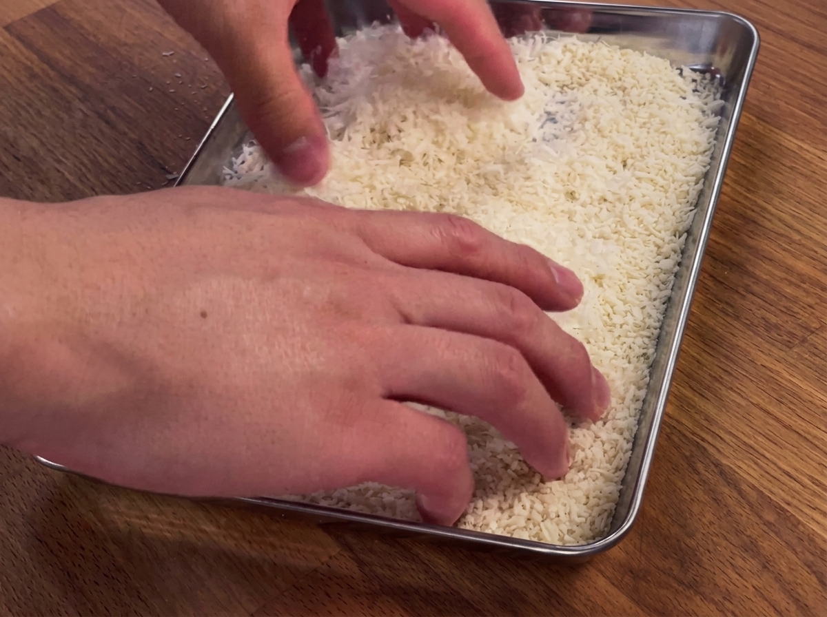 Hände drücken eine Hähnchenbrust in eine Schale mit Paniermehl und Parmesan.