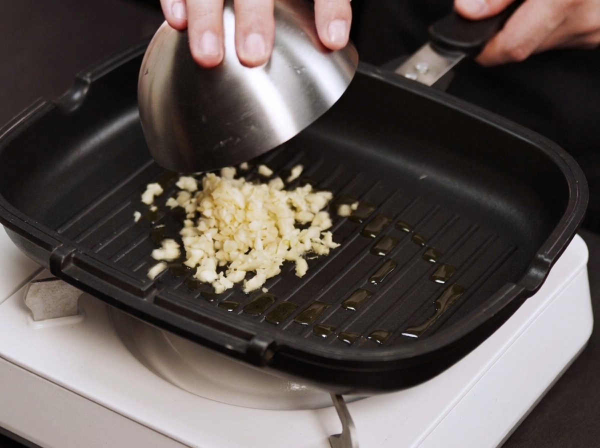 Fein gehackter Knoblauch und Zwiebelwürfel brutzeln in einer heißen Pfanne.
