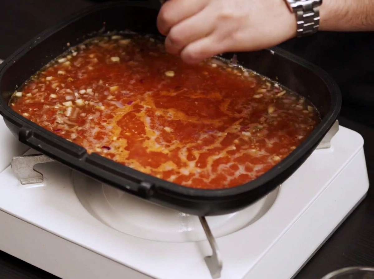 Eine Pfanne mit köchelnder Tomatensauce wird mit Salz und Pfeffer gewürzt.