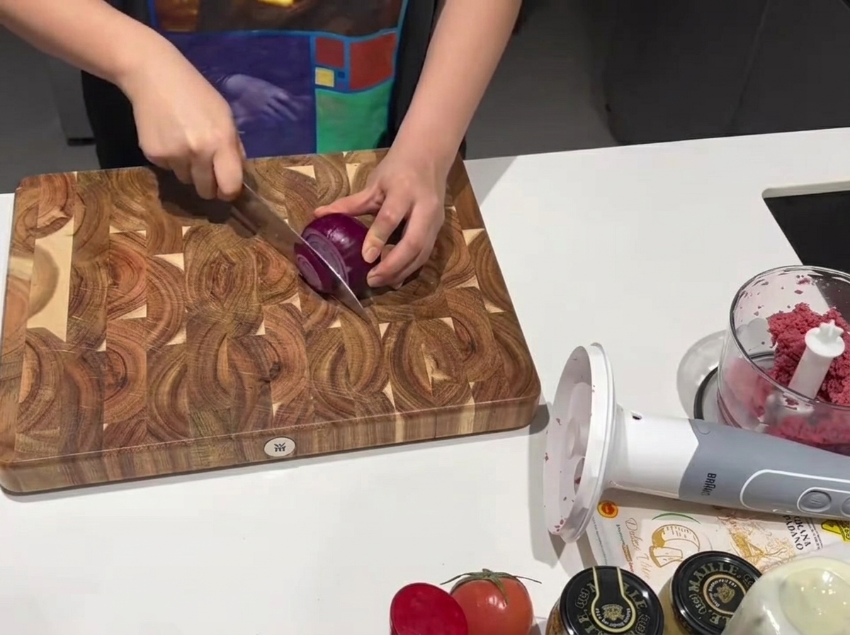 Ein scharfes Küchenmesser schneidet eine rote Zwiebel auf einem Holzbrett.