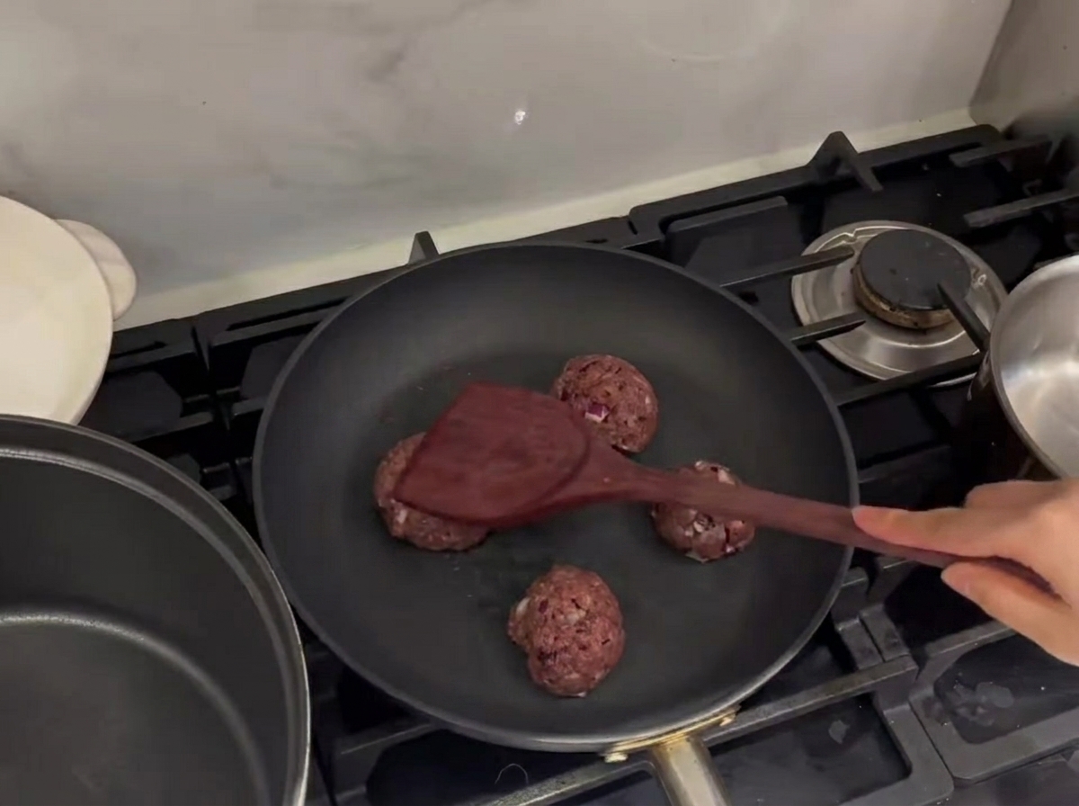 Hackfleischbällchen werden in der Pfanne mit einem Metallspatel flach gedrückt.
