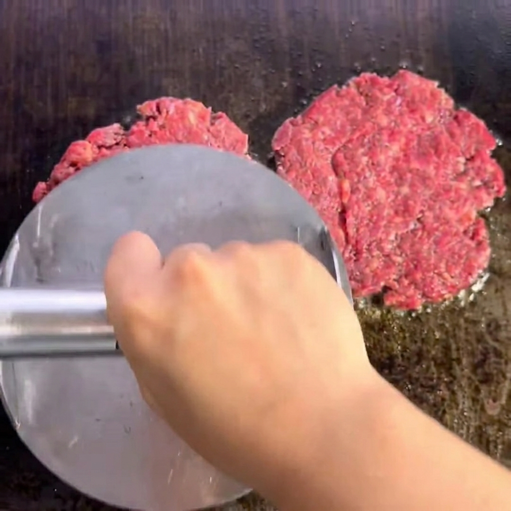 Zwei gewürzte Rinder-Patties brutzeln auf dem Grill und zeigen eine braune, angebratene Kruste.