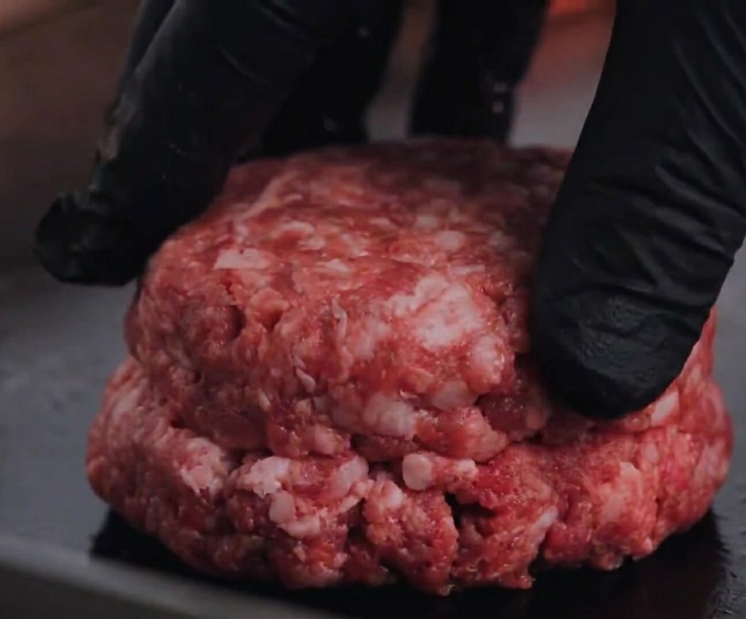 Ein rohes Angus-Rindfleisch-Patty wird auf einen heißen Grill gedrückt.