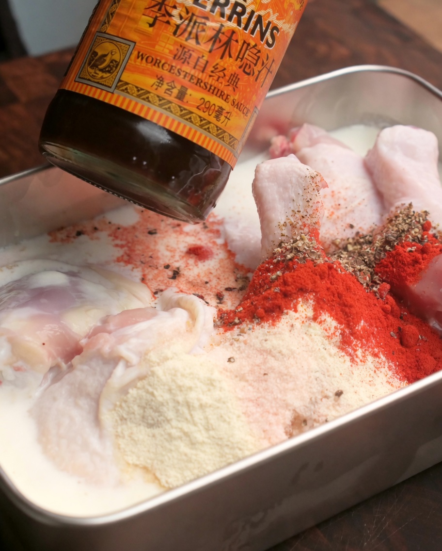 Worcestershiresauce wird über marinierte, mit roten Gewürzen bestreute Hähnchenkeulen geträufelt.