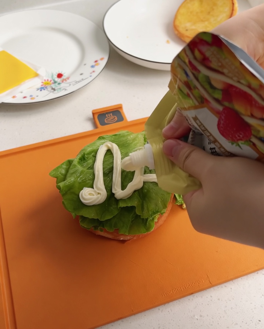 Weißes Salat-Dressing wird aus einem Beutel in Zickzack-Linien auf den Salat gegeben.