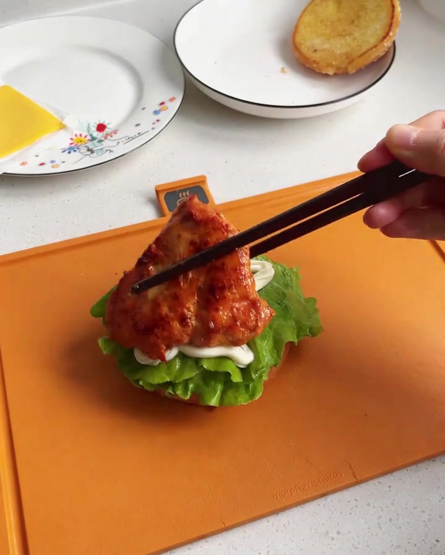 Ein Stück gebratenes, glasiertes Hähnchen wird auf das Bun-Unterteil mit Salat und Dressing gesetzt.