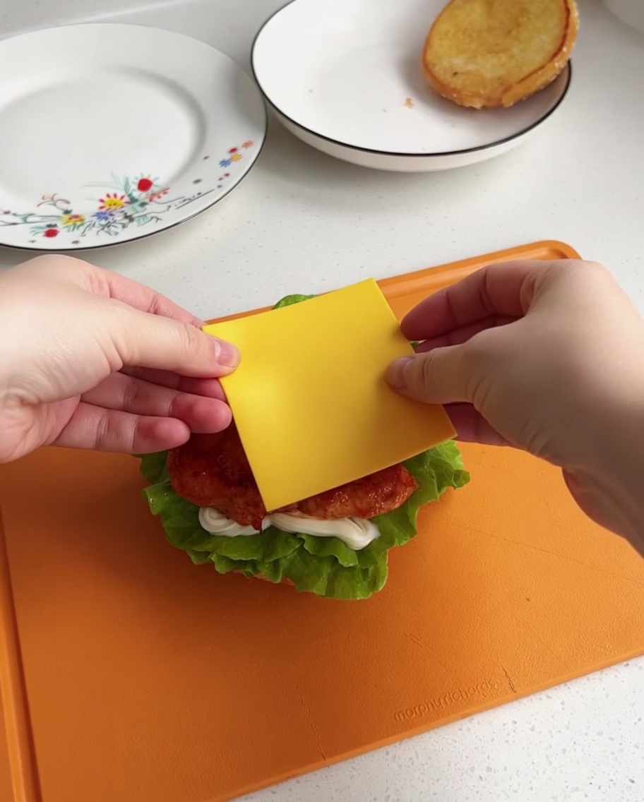 Eine Scheibe gelber Käse wird auf das heiße Hähnchenstück gelegt.