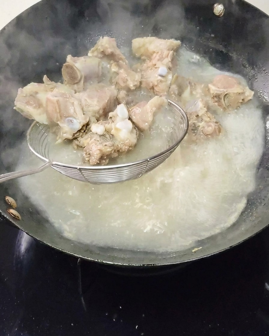 Blanchierte Schweinerippchen werden mit einem Schaumlöffel aus dem kochenden Wasser gehoben.