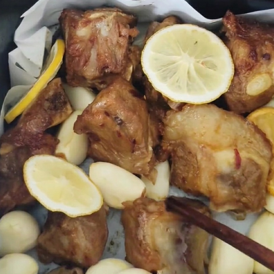 Schweinerippchen werden im Heißluftfritteuse gewendet und mit Honigglasur bestrichen, geröstete Knoblauchzehen sind sichtbar.