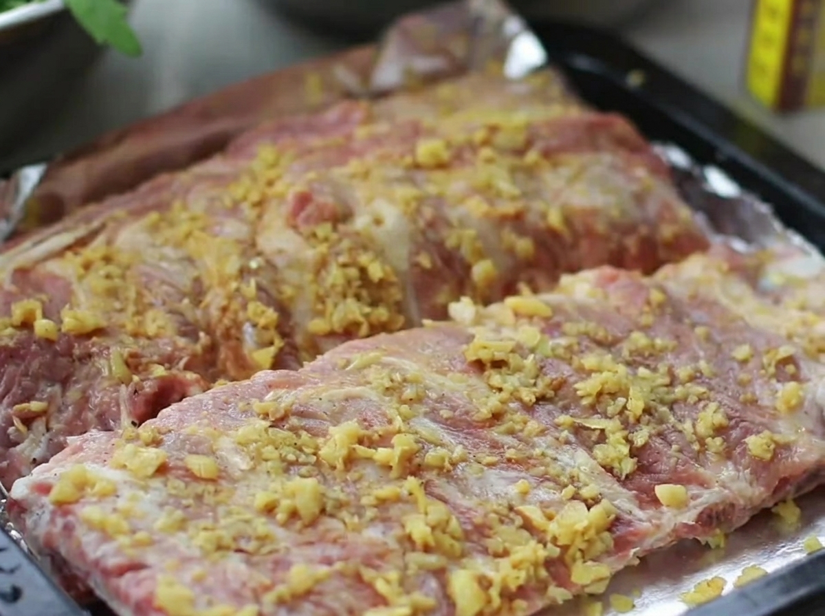 Ein Backblech mit gewürzten Rippchen, fest eingewickelt in glänzende Alufolie.