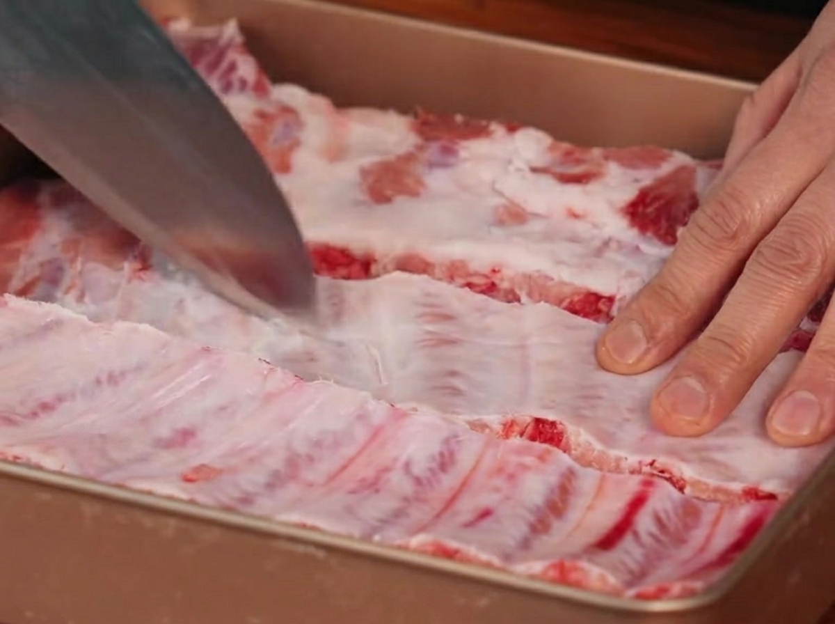 Ein Messer schneidet die Silberhaut auf der Rückseite der Schweinerippchen ein.