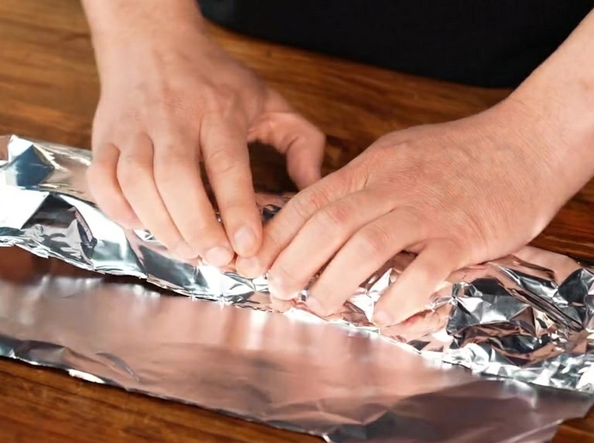 Gewürzte Schweinerippchen werden fest in ein Stück Aluminiumfolie eingewickelt.