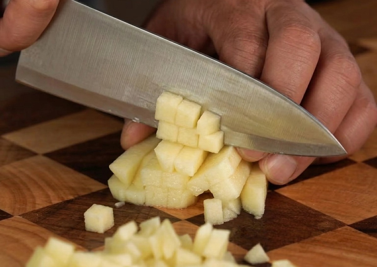Ein frischer Apfel wird auf einem Holzschneidebrett sorgfältig in kleine, gleichmäßige Würfel geschnitten.