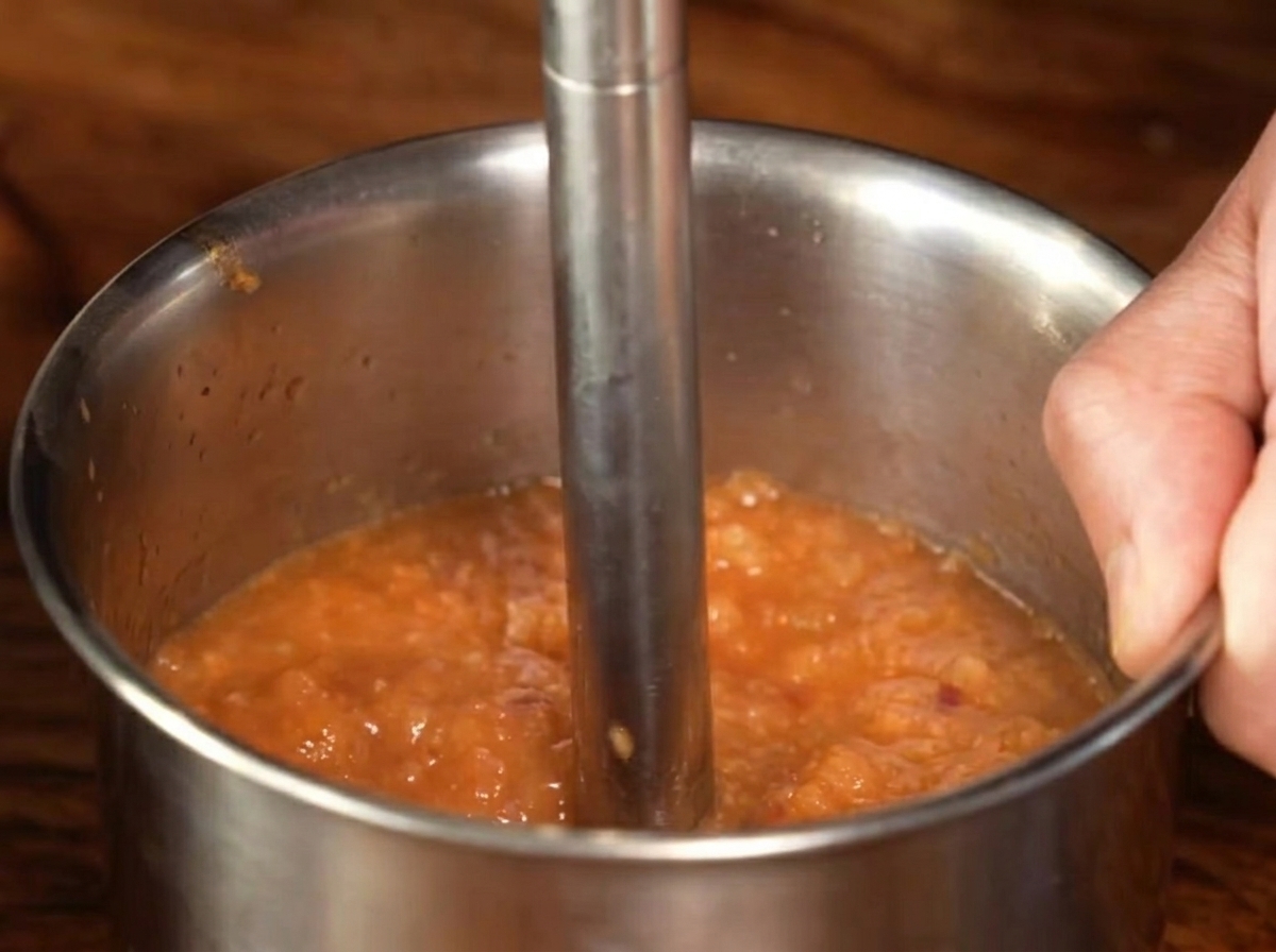 Ein Stabmixer aus Metall püriert die gekochte Saucenmischung zu einem feinen Püree.
