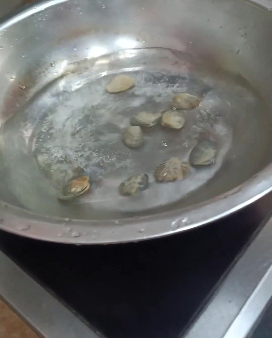 Muscheln kochen in einem Topf mit Wasser, die Schalen beginnen sich zu öffnen.