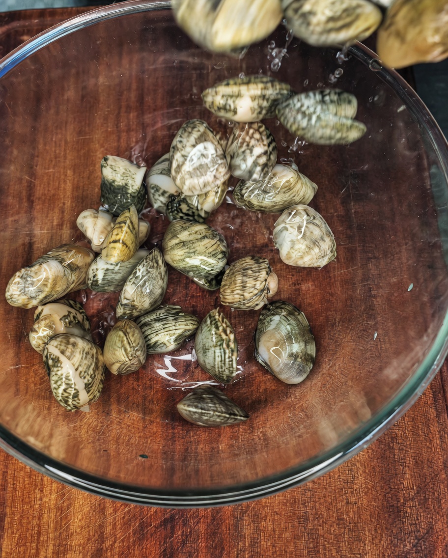 Frische Muscheln in einer Glasschüssel mit Wasser, Salz und etwas Öl.