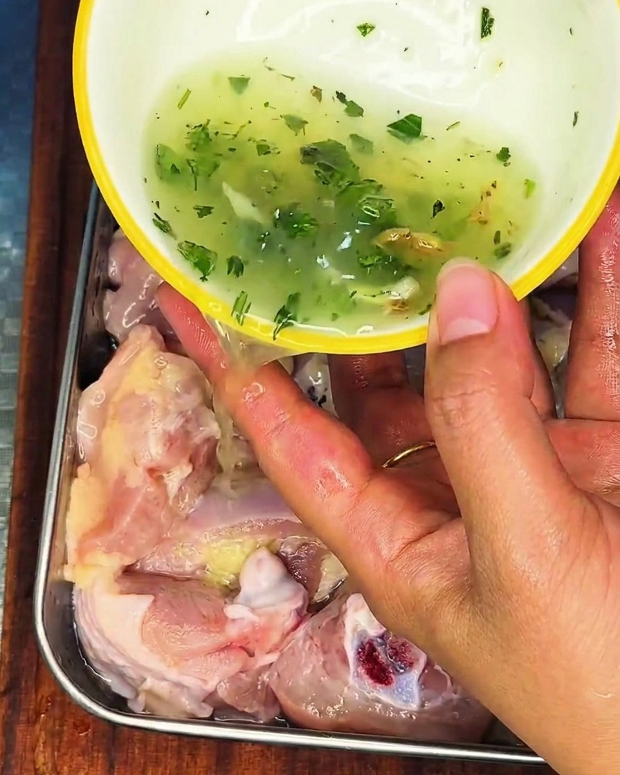 Frühlingszwiebel-Ingwer-Flüssigkeit wird über rohes Hähnchen in einer Edelstahlschale gegossen.