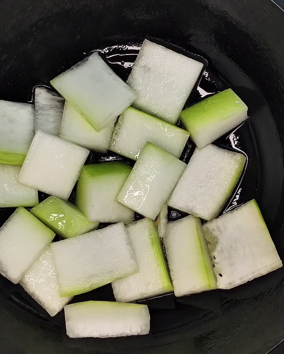 Geschnittene Wintermelone bedeckt den Boden eines schwarzen Topfes.