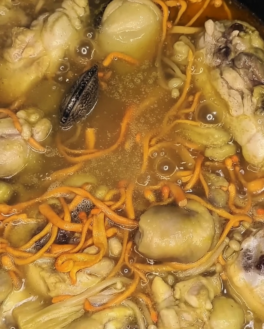 Frische Muscheln werden auf dem garenden Hähnchen und Gemüse im Topf platziert.