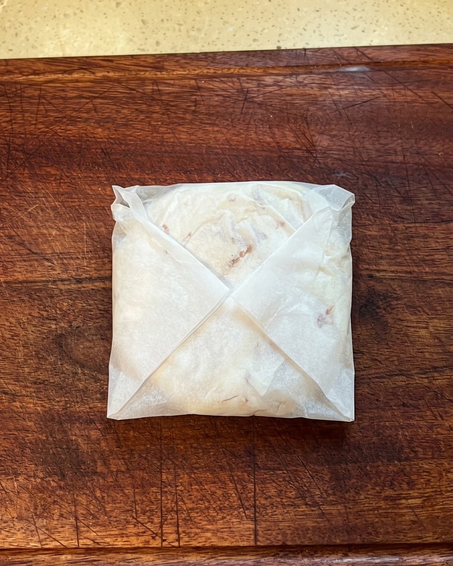 Der gefaltete Pfannkuchen in Backpapier eingewickelt und auf einem Holzbrett flach gedrückt.