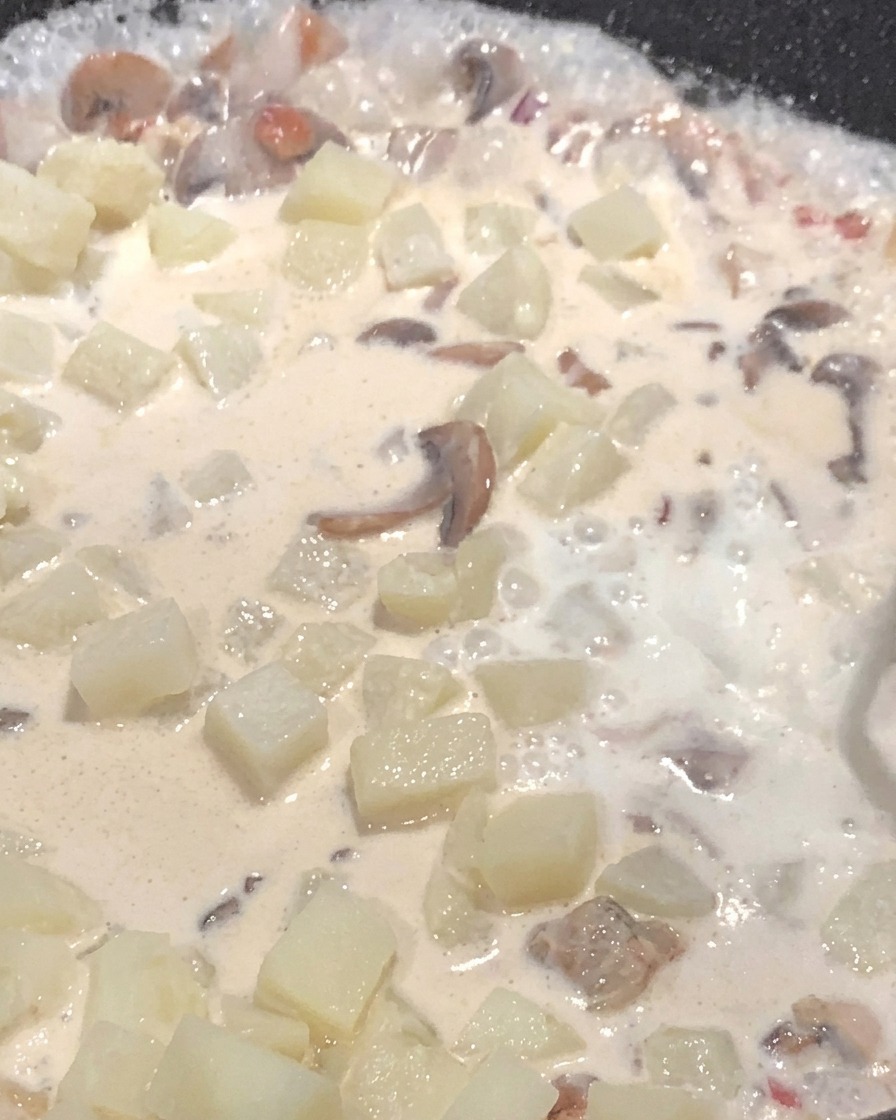 Milch wird in die Pfanne mit Kartoffeln und Pilzen gegossen, während alles in einer cremigen Sauce simmert.