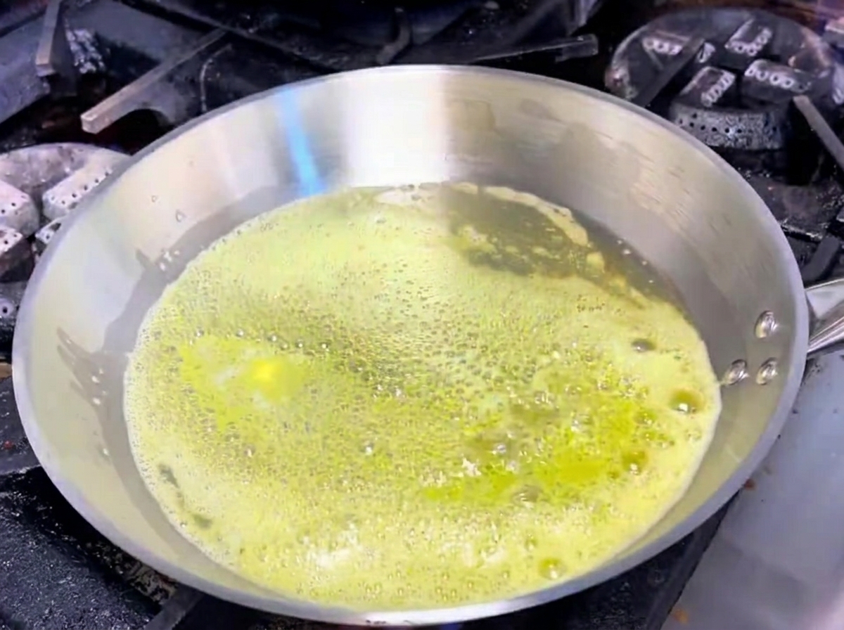 In Butter schmorender Knoblauch und Schalotten in einer Edelstahlpfanne.