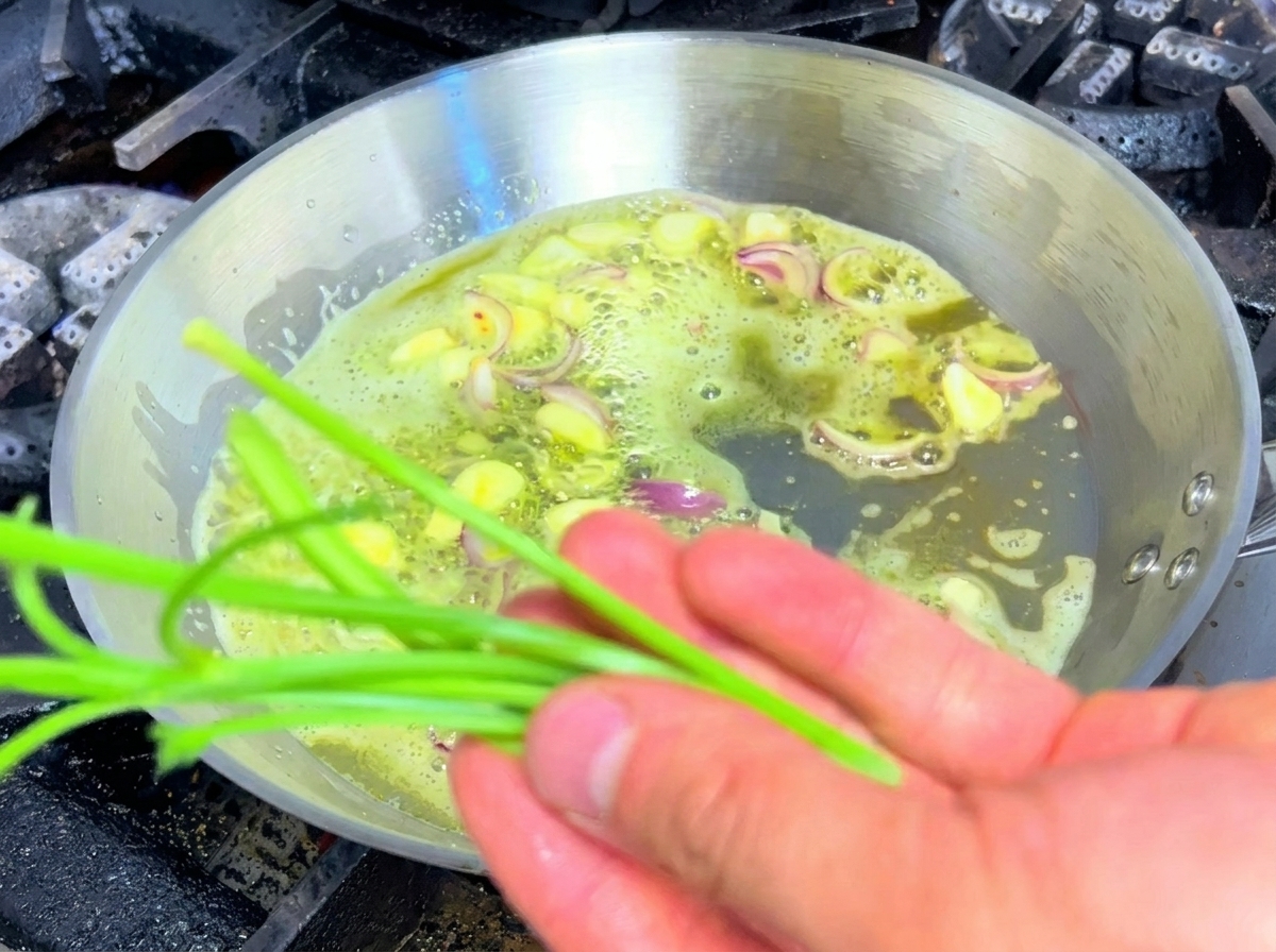 Petersilienstiele werden zusammen mit Knoblauch und Schalotten in einer Pfanne angebraten.