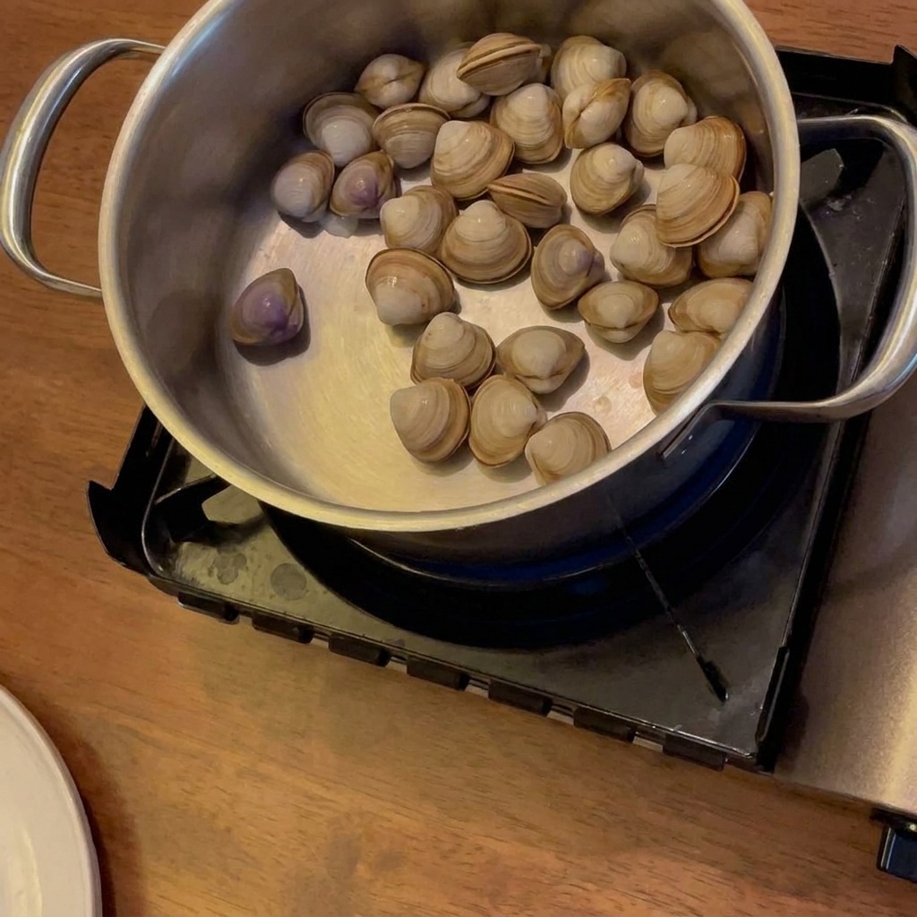 Alkohol wird in einen Topf mit Muscheln, Kartoffeln und Karotten gegossen, während dieser auf einem mobilen Gaskocher steht.